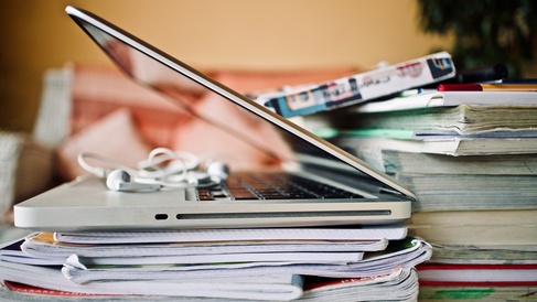 A laptop perched atop a pile of books and journals