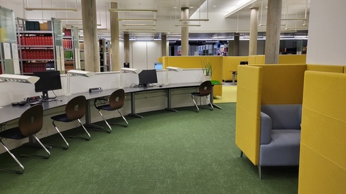 A section of the lower ground floor of the Moore library, showing desk spaces, library computers and some cushioned, yellow study pods